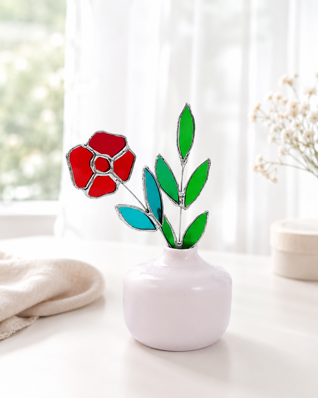 گل شیشه ای قرمز با برگ فیروزه ای و شاخه ای از برگ سبز در گلدان صورتی روی زمینه سفید